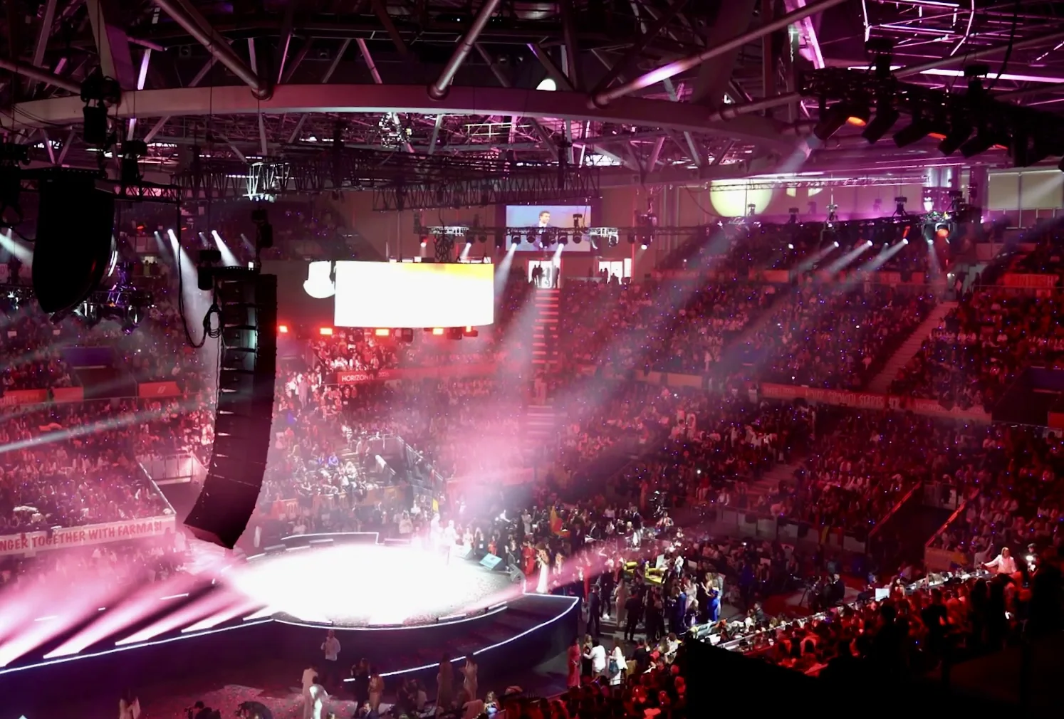 Arena event with a full audience and pink stage lighting